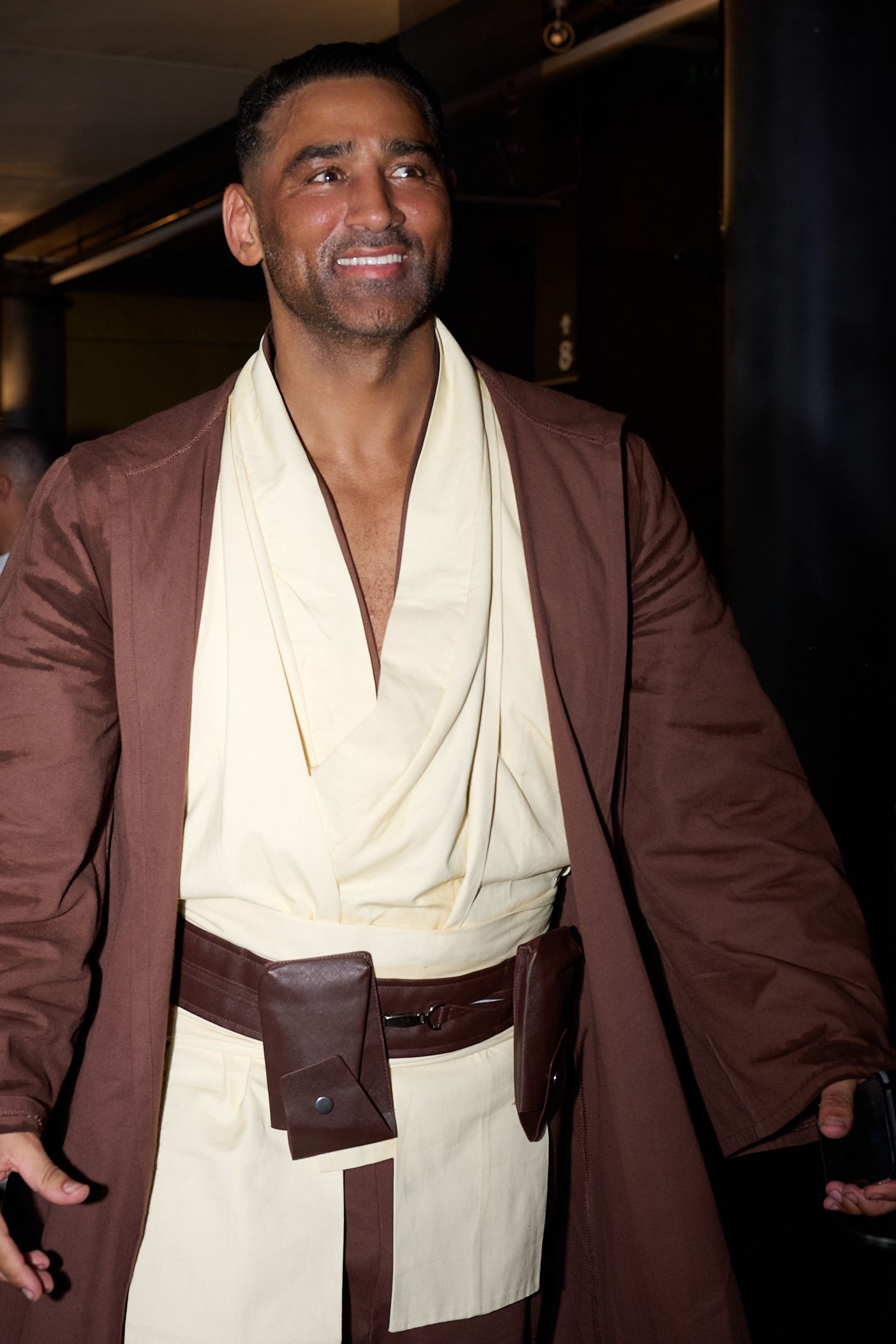 Man wearing a Jedi costume with brown robe and cream tunic with leather belt at a Star Wars themed event.