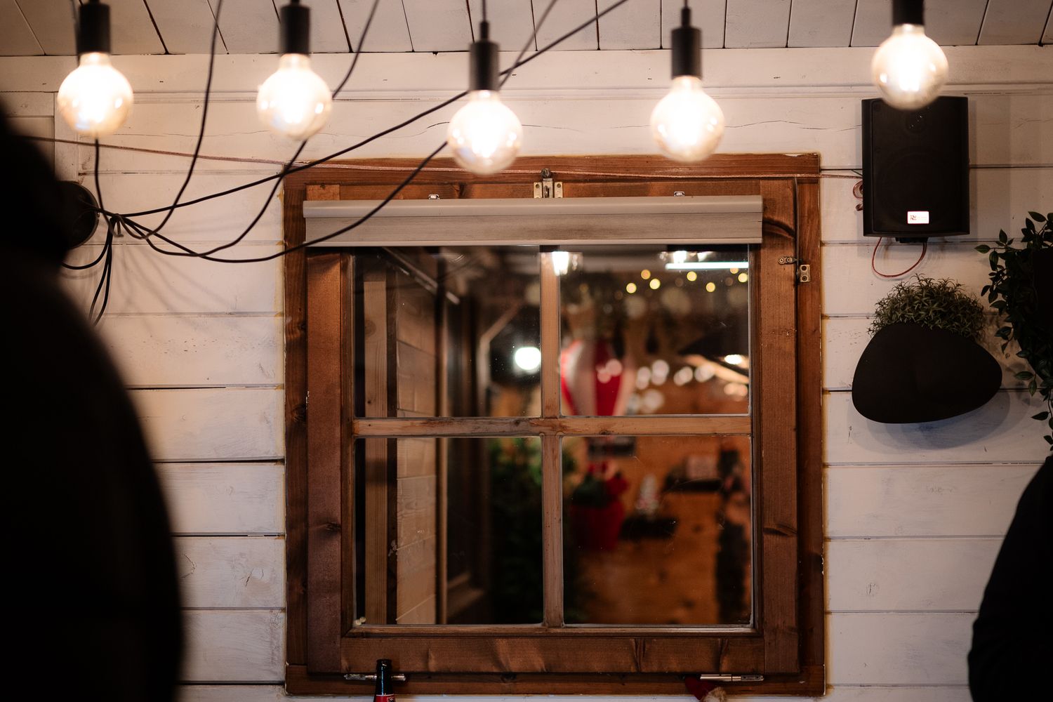 Rustic wooden framed mirror on white shiplap wall with Edison bulb string lights in a cozy cafe interior.