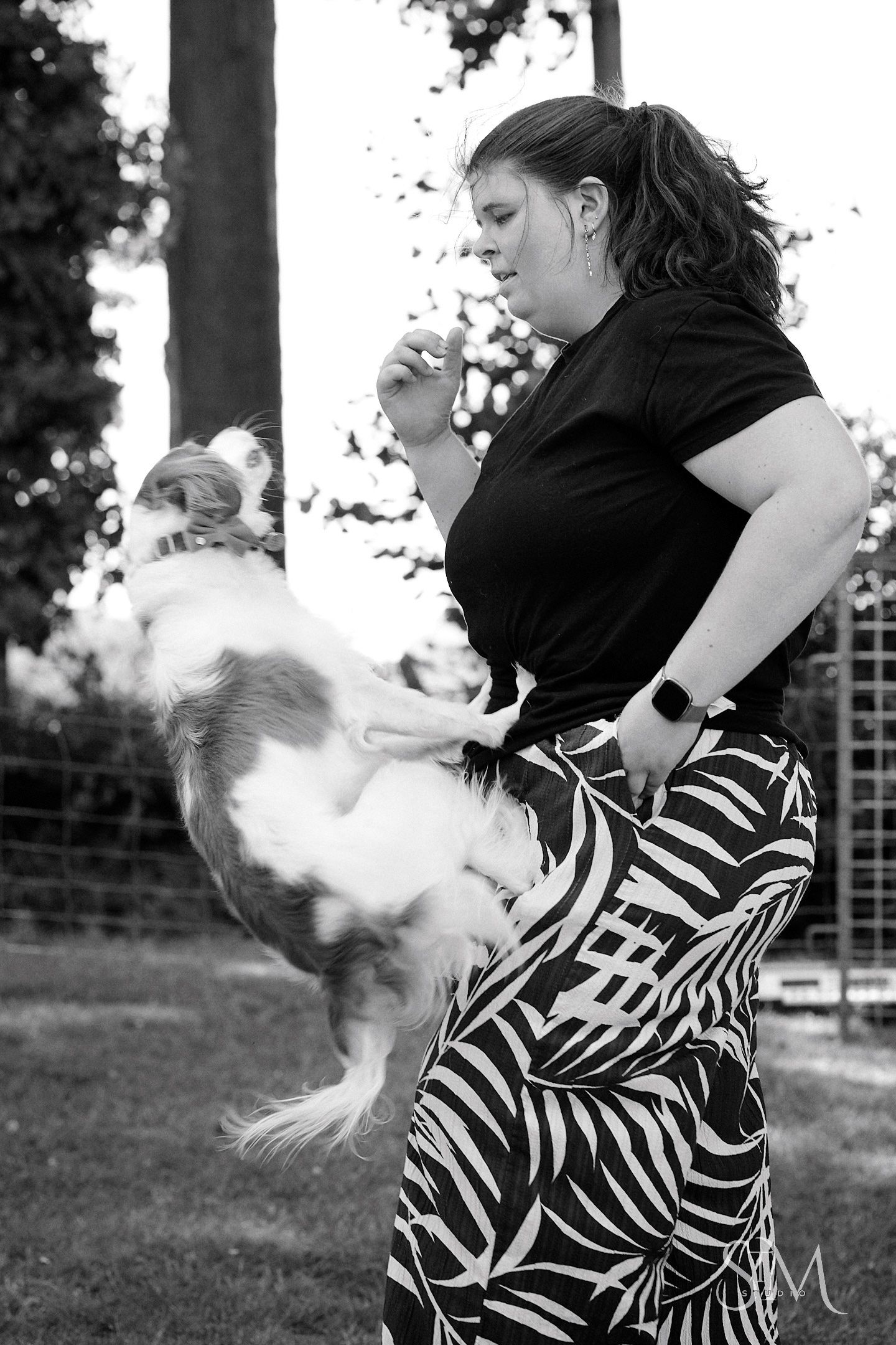 Woman in zebra print pants trains small fluffy dog outdoors in black and white photo.