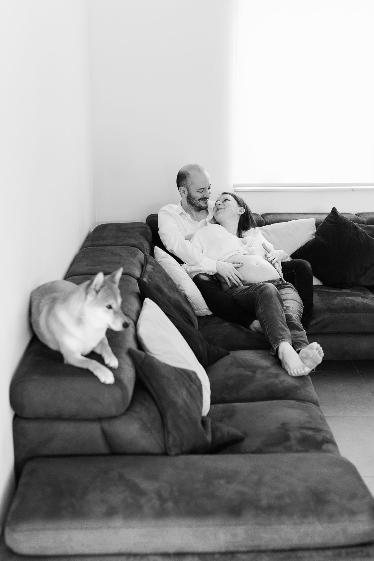 Black and white photo of a couple relaxing on a large sofa with a Husky dog beside them.