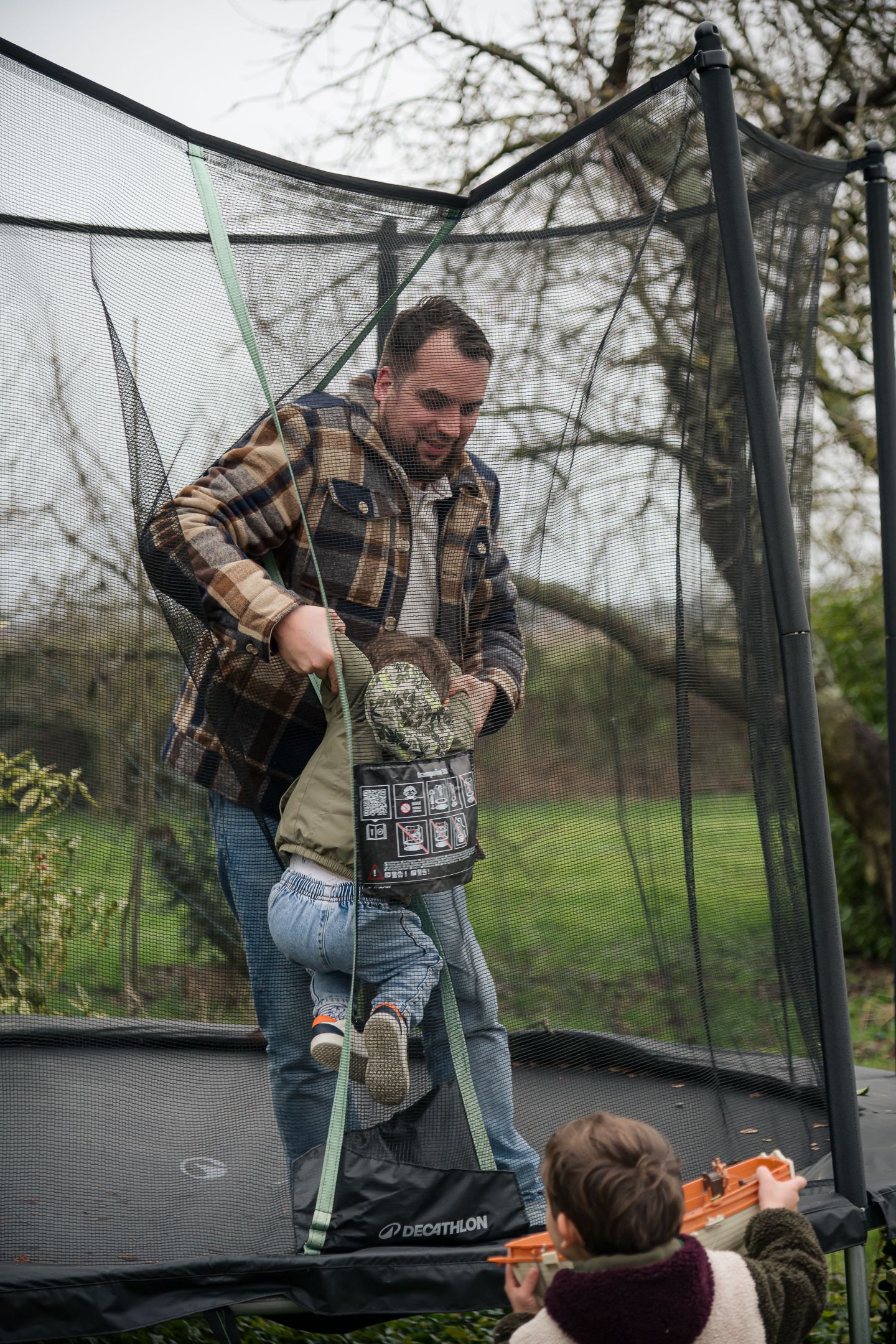 Father helping young child climb off a trampoline in an autumn garden.