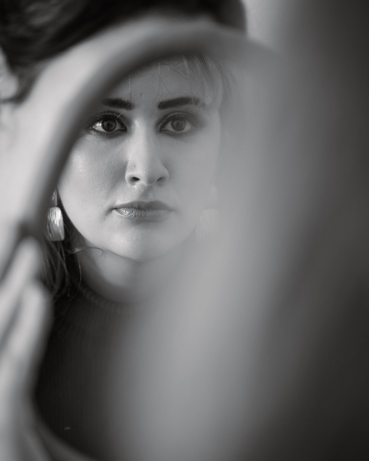 Black and white portrait of a woman with hoop earrings reflected in a mirror.