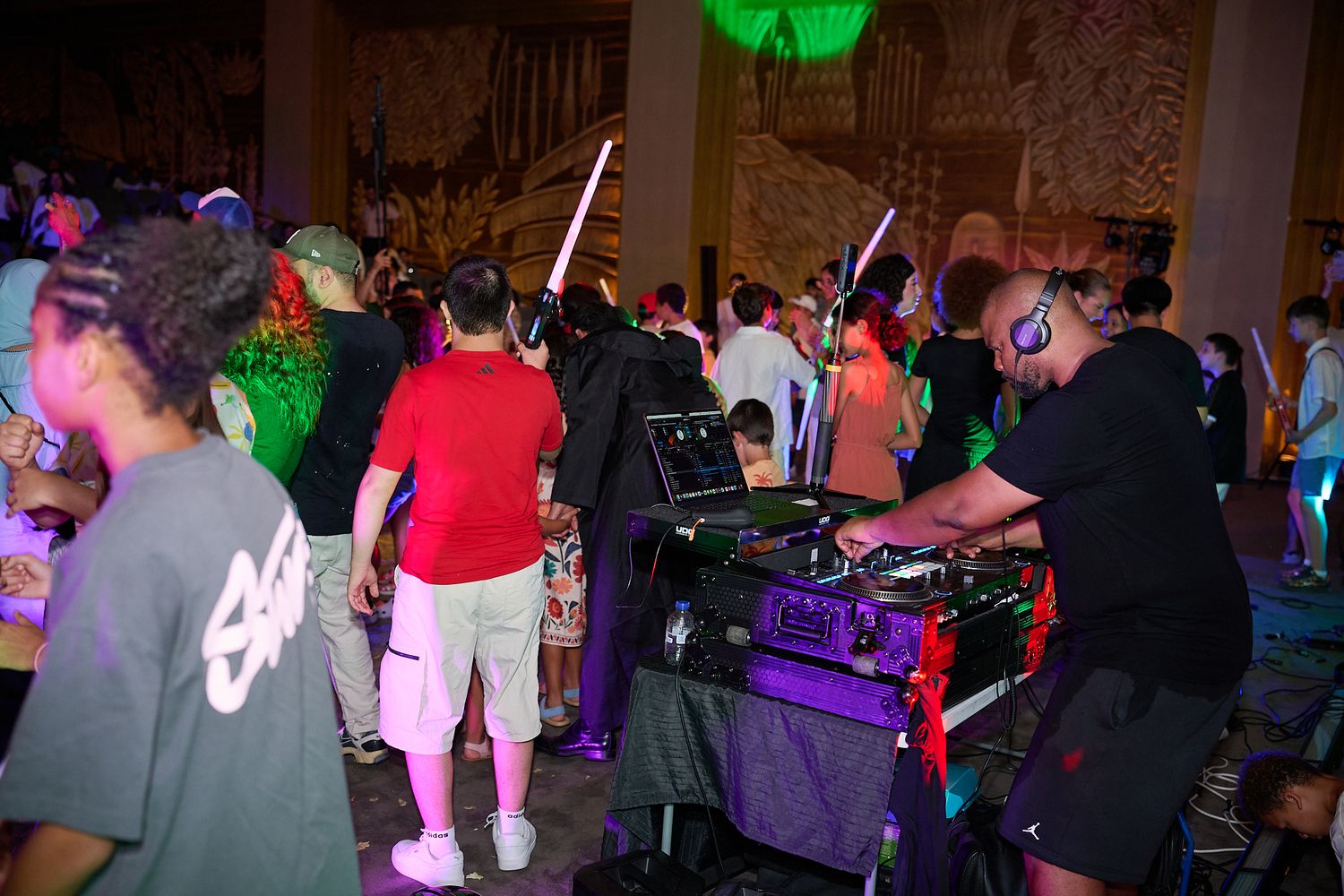 DJ performing at a lively indoor party with colorful lights and a crowd of dancing guests.