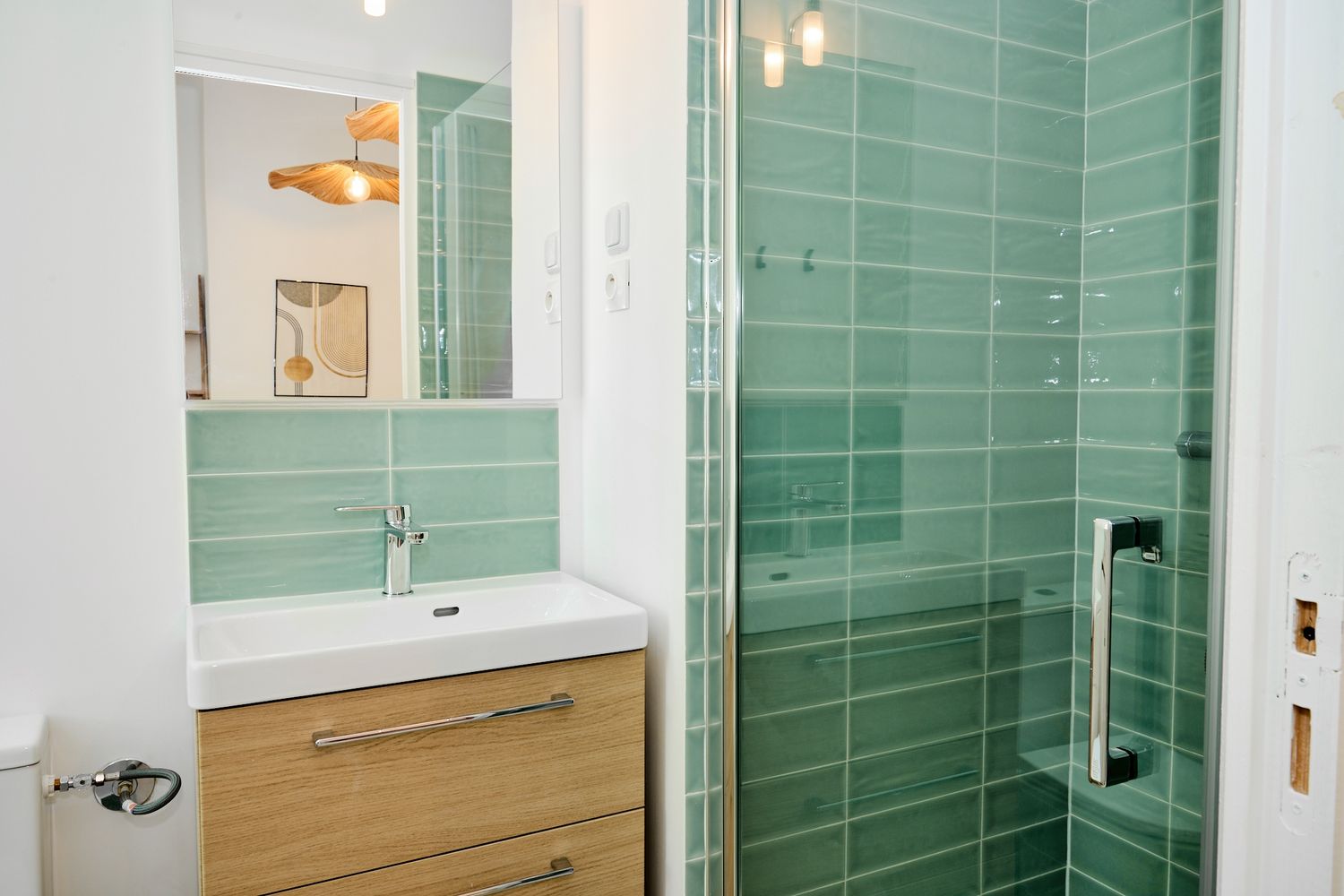 Modern bathroom with green subway tiles, glass shower, wooden vanity, and white sink.