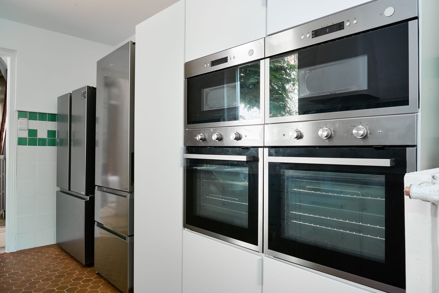 Sleek kitchen featuring stainless steel double ovens, microwave, and refrigerator with white cabinetry.