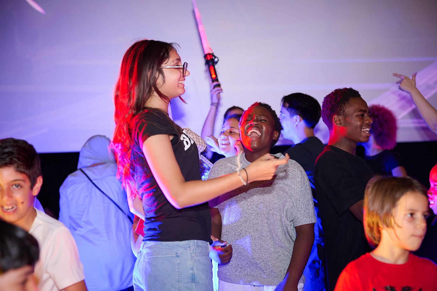 Teens enjoying a lively party event with colorful LED lights, dancing and holding glow sticks indoors.