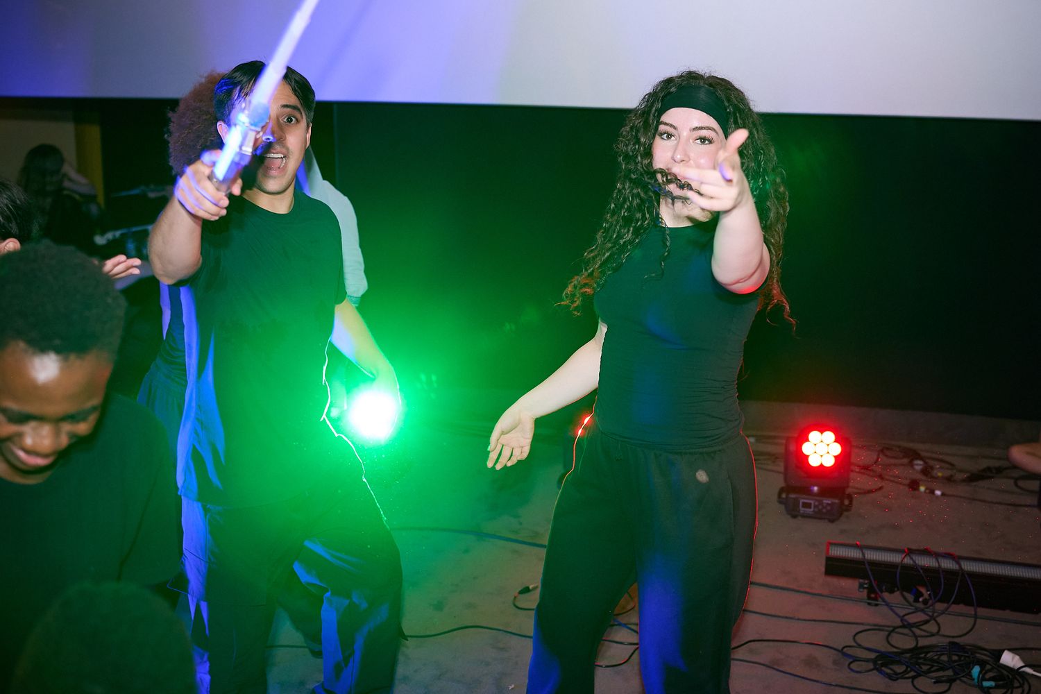 Performers dancing on stage with green and blue laser lights during a live music event.