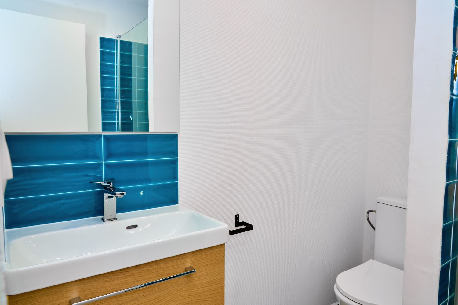 Modern bathroom with white vanity, chrome faucet, and vibrant blue tile backsplash above a white sink with toilet.