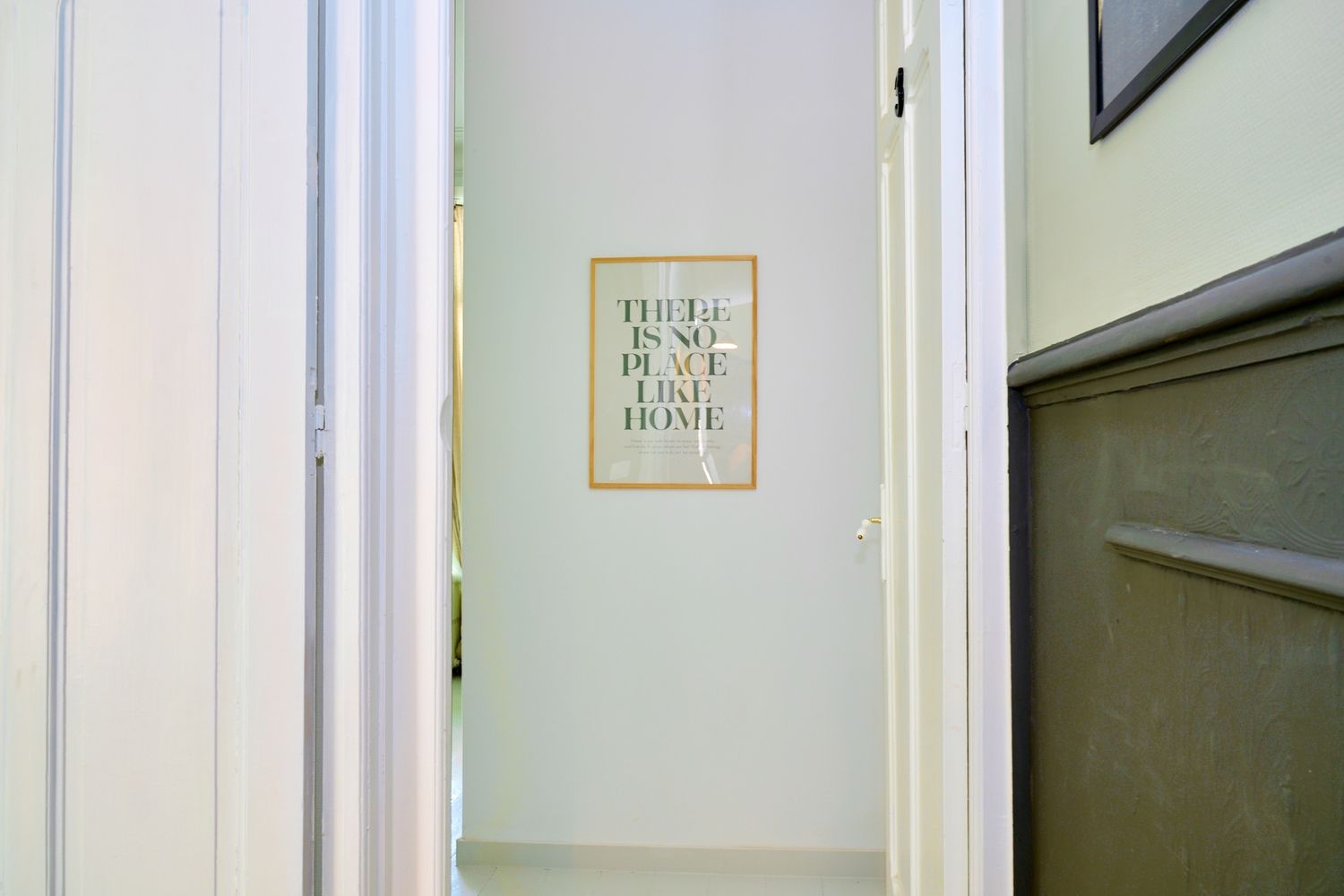 Bright hallway with white doors leading to a room with a 'There Is No Place Like Home' framed wall sign.