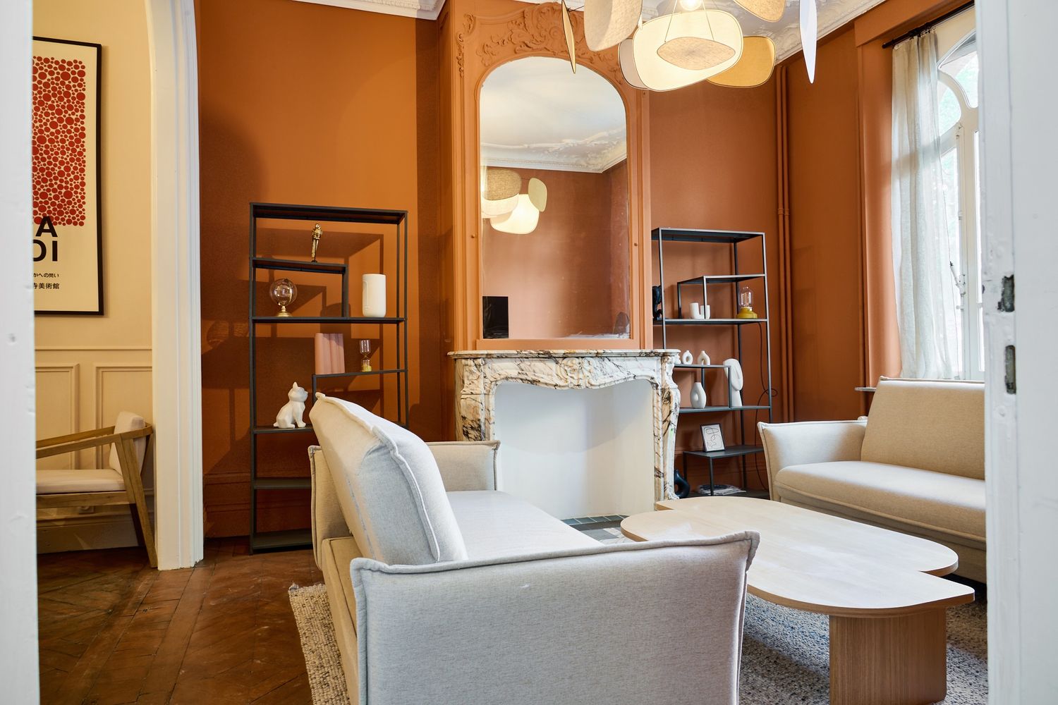 Elegant living room with terracotta walls, white fireplace, gray sofas, herringbone floors, and modern pendant lights.