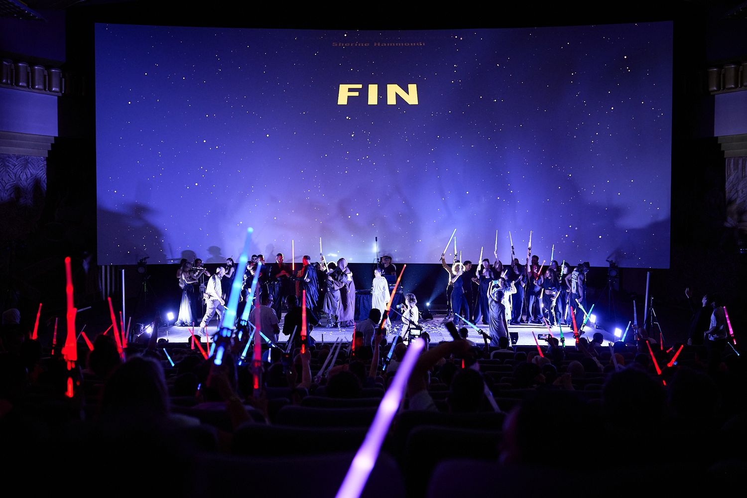 Star Wars cosplayers on stage with colorful lightsabers at a cinema event with FIN displayed on screen.