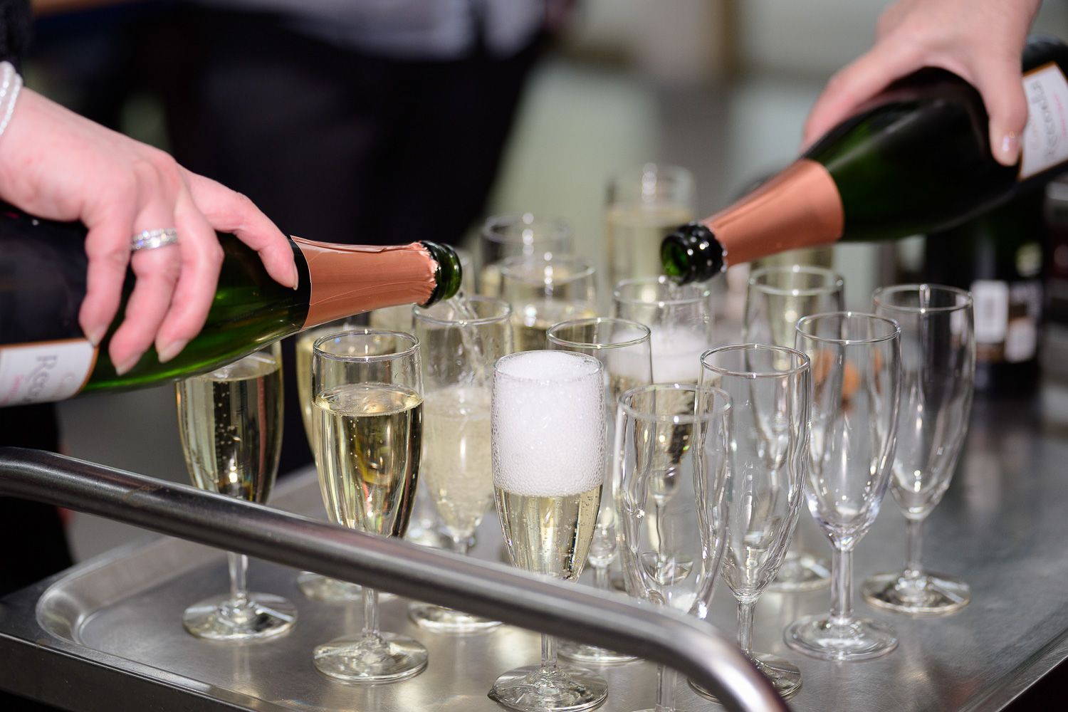 Two servers pouring champagne into elegant flute glasses on a silver tray at a formal celebration event.