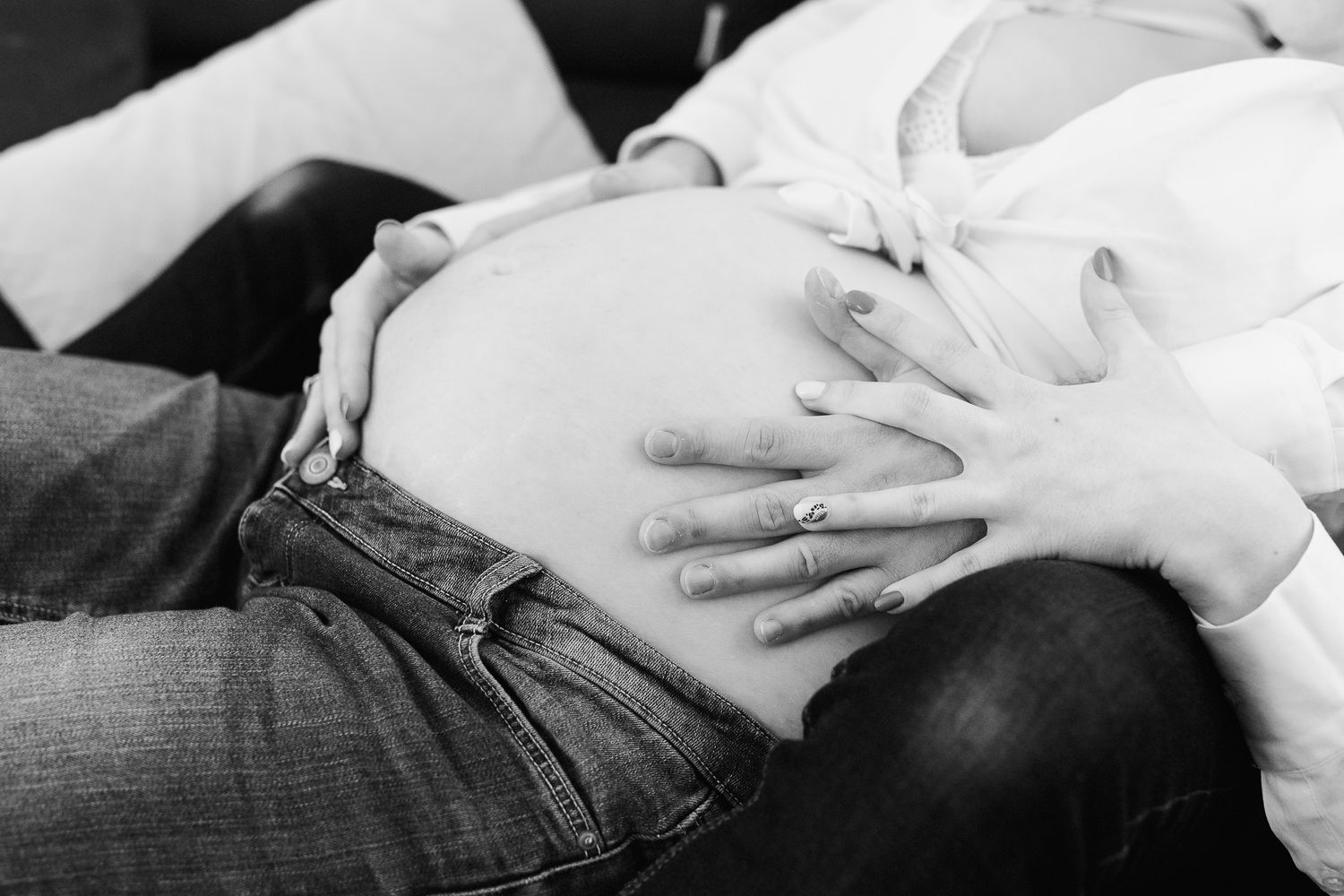 Black and white photo of pregnant woman in jeans with hands cradling baby bump.