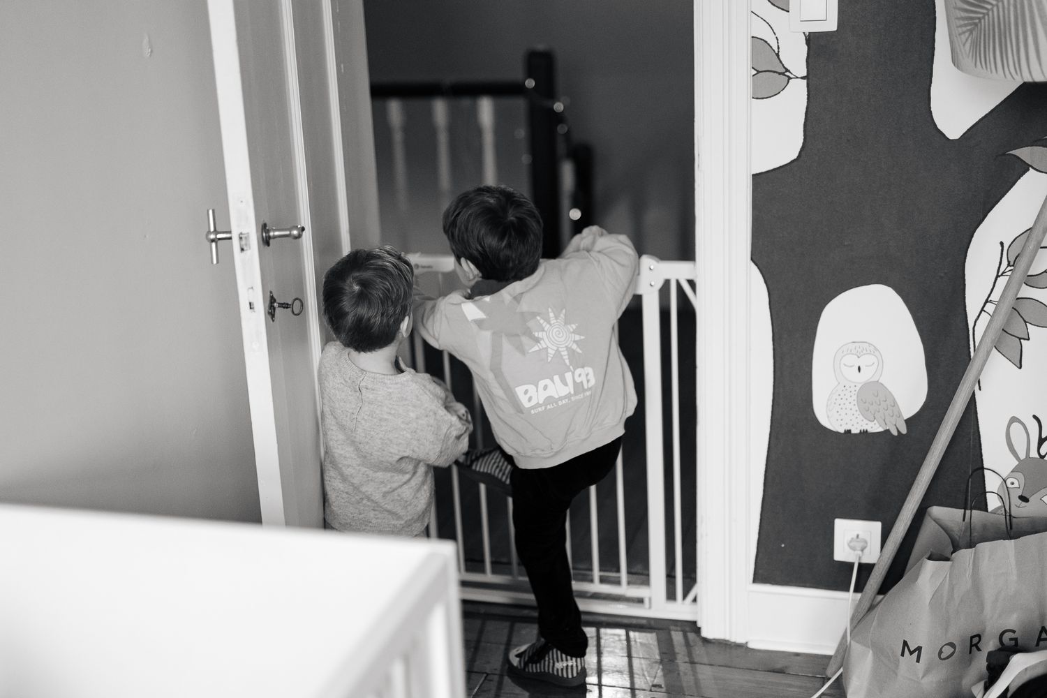 Two young children hugging near a stair gate in a black and white home photo.