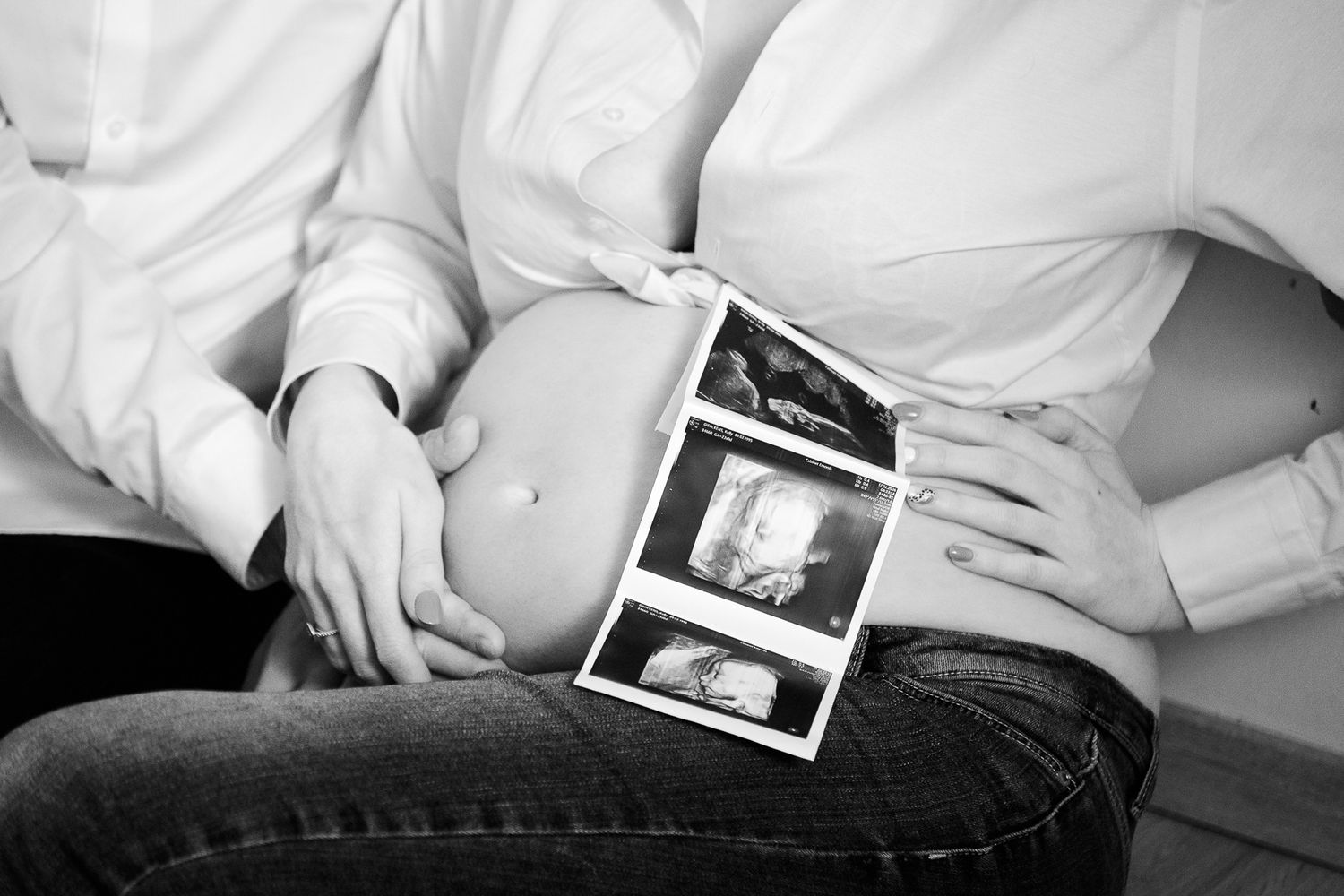 Black and white photo of pregnant woman with partner holding ultrasound scans against baby bump.