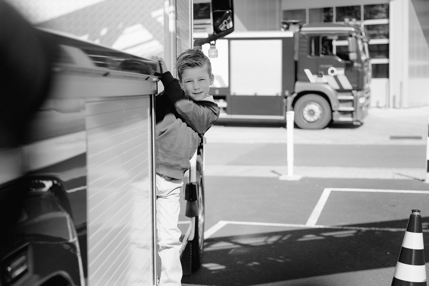 A young boy leans against a large vehicle at a truck depot in this black and white photo.