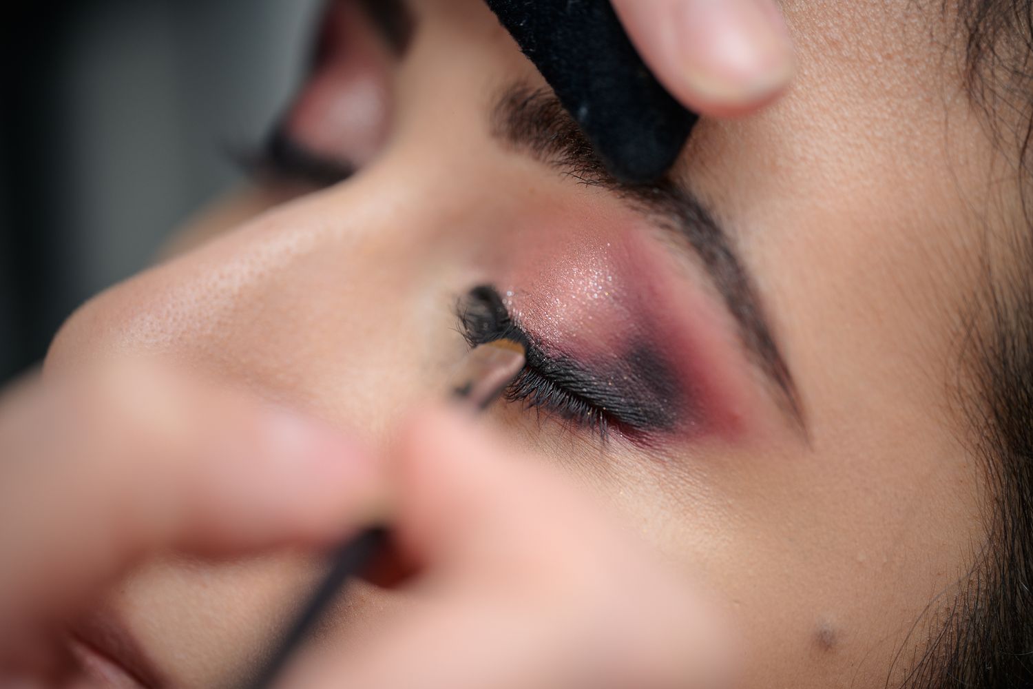 Close-up of a makeup artist applying dramatic red and black eyeshadow on a woman's eye with a brush.