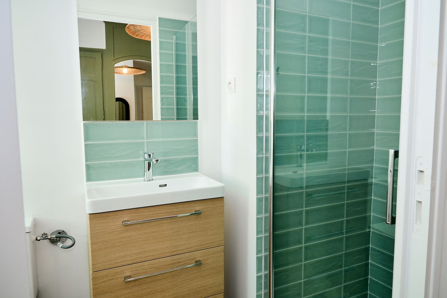 Modern bathroom with green subway tile shower, wood vanity, white sink, and mirror in a clean, minimalist design.