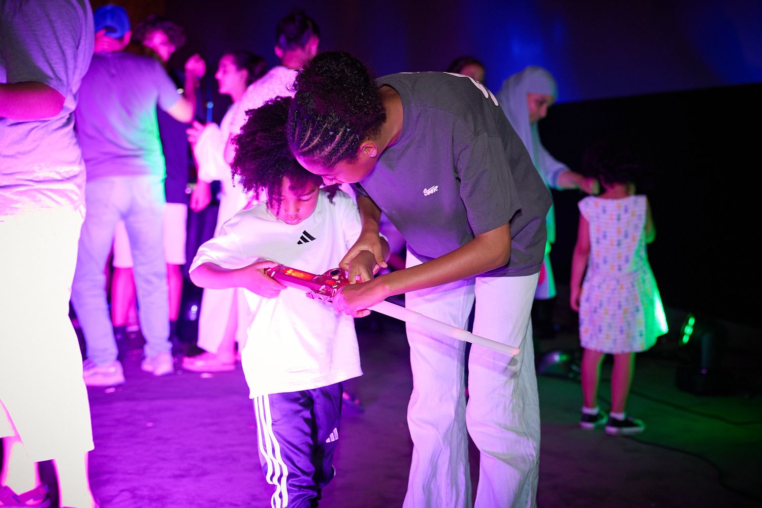 Adult and child dancing together at a colorful neon-lit party event with other guests in the background.