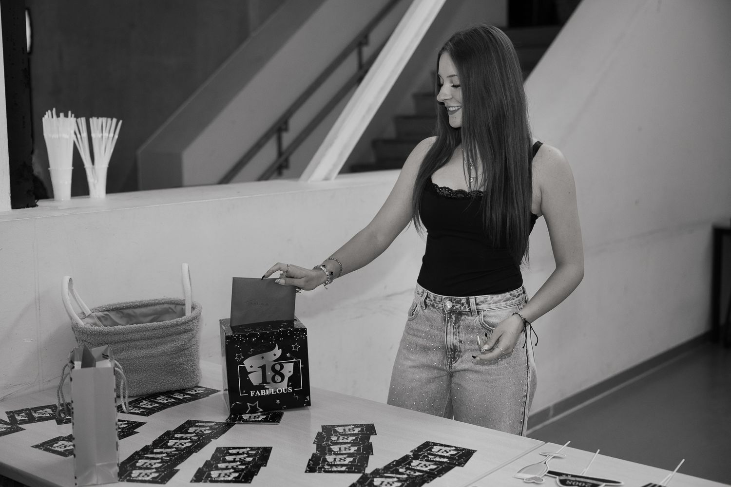 Young woman in black top and jeans reaching for items on a decorated table in black and white.
