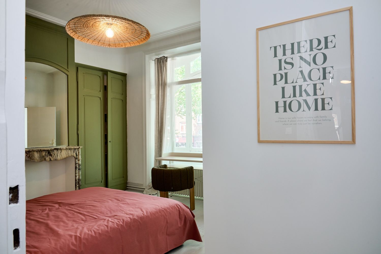 Cozy bedroom with green wardrobe, red bedding, and a framed 'There Is No Place Like Home' wall art print.
