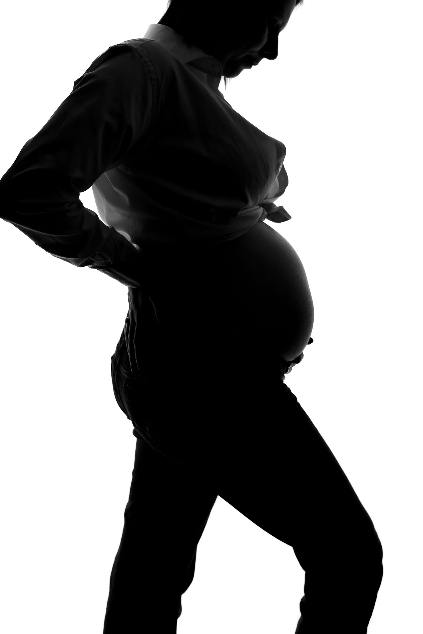 Black and white silhouette of a pregnant woman standing sideways, cradling her baby bump with both hands.