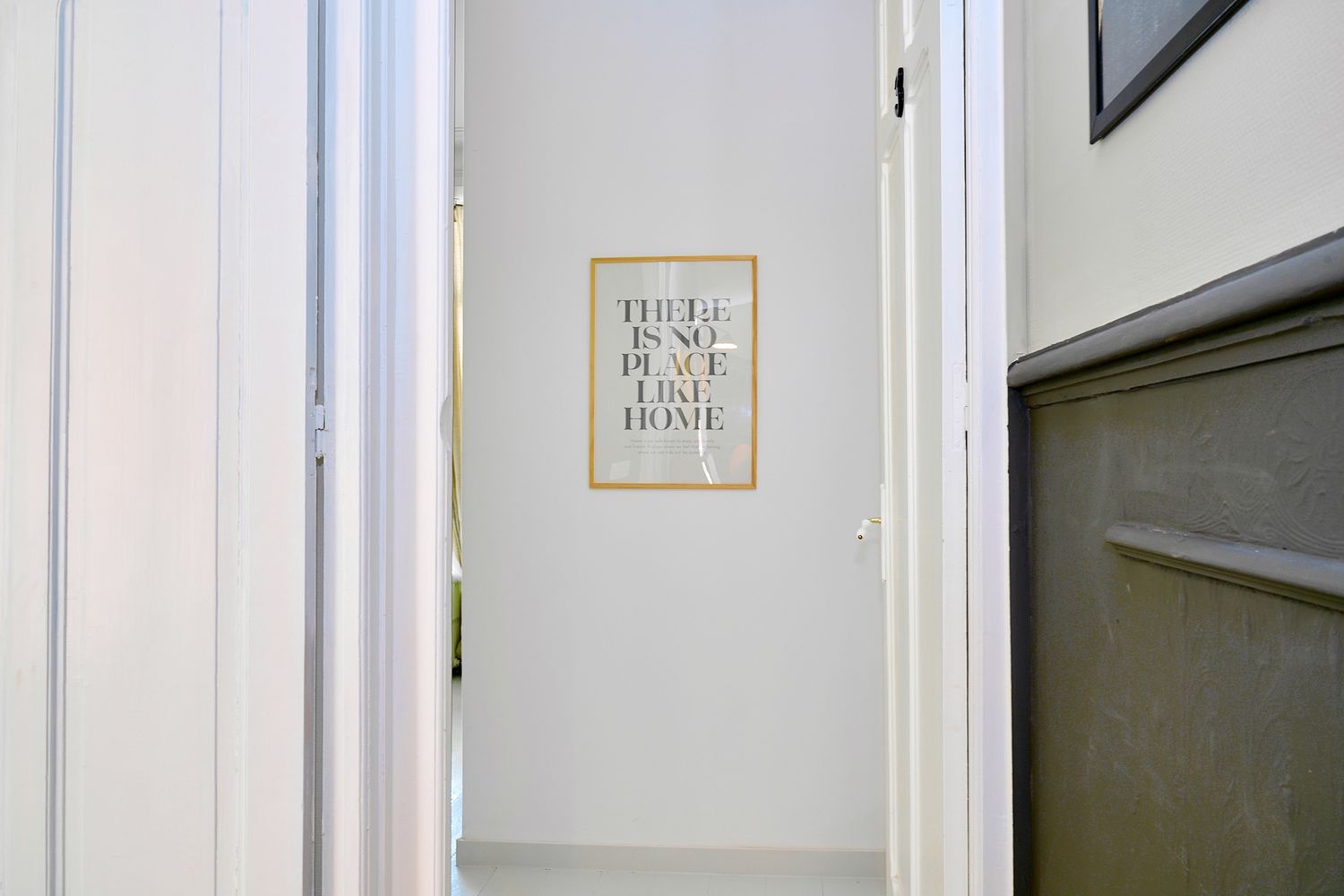 Bright hallway with white walls leading to a framed 'There Is No Place Like Home' sign on the wall.