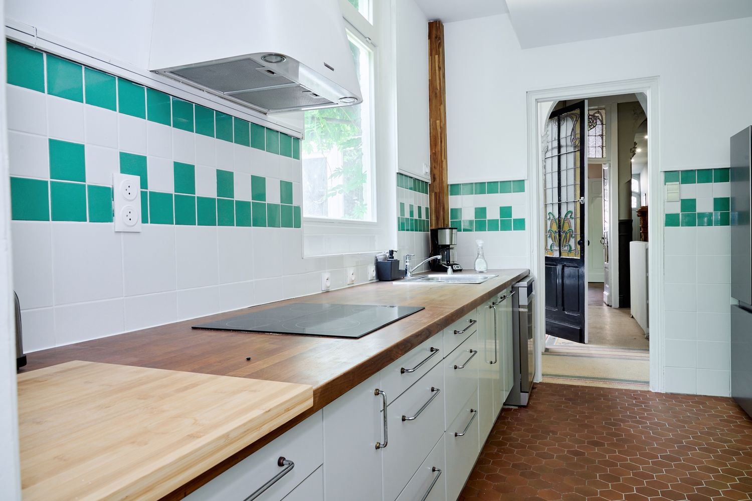 Modern kitchen with green and white tile backsplash, wooden countertops, and induction cooktop in a bright space.