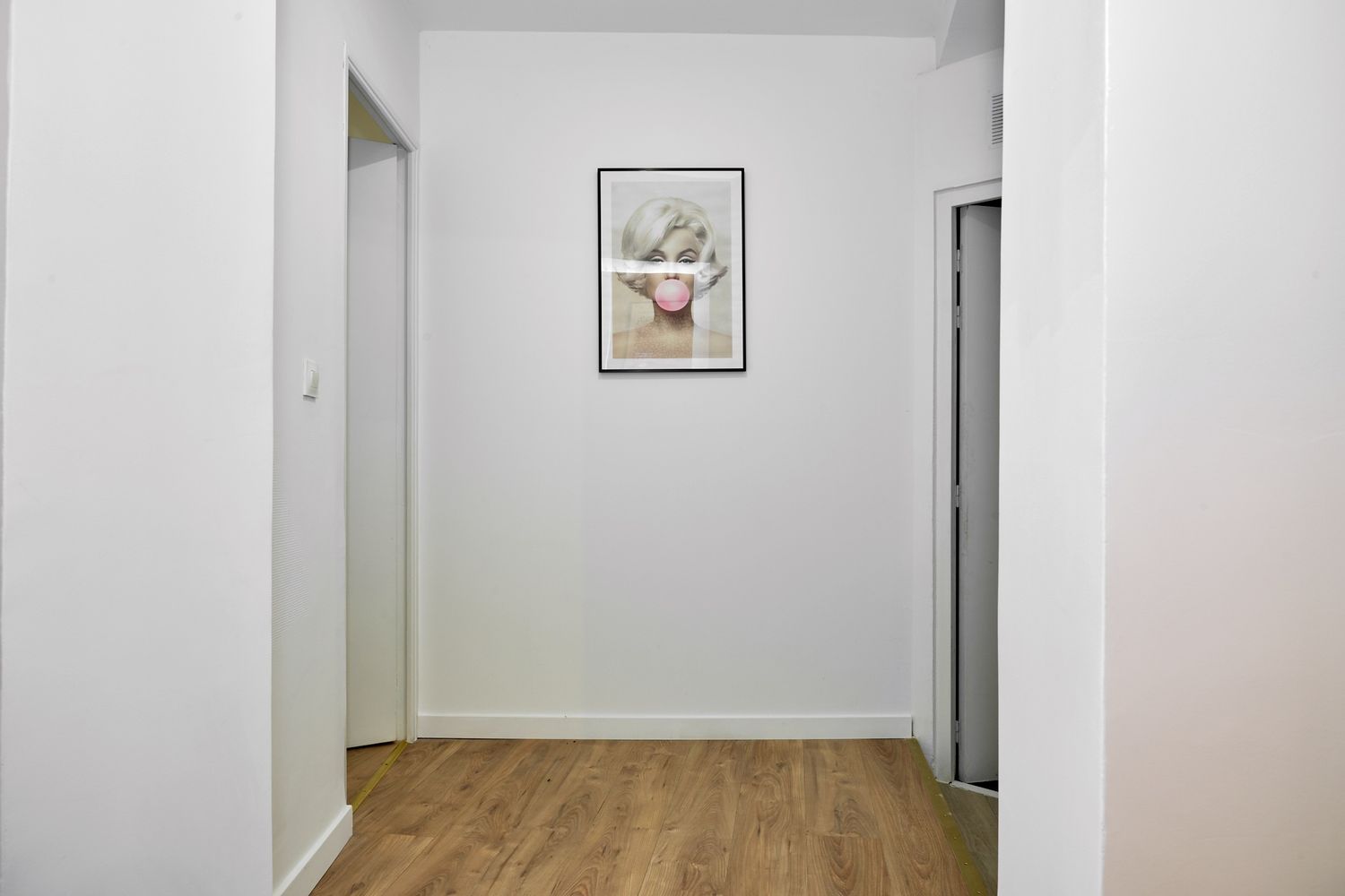Bright hallway with hardwood floors, white walls, and a framed floral artwork, leading to multiple rooms.