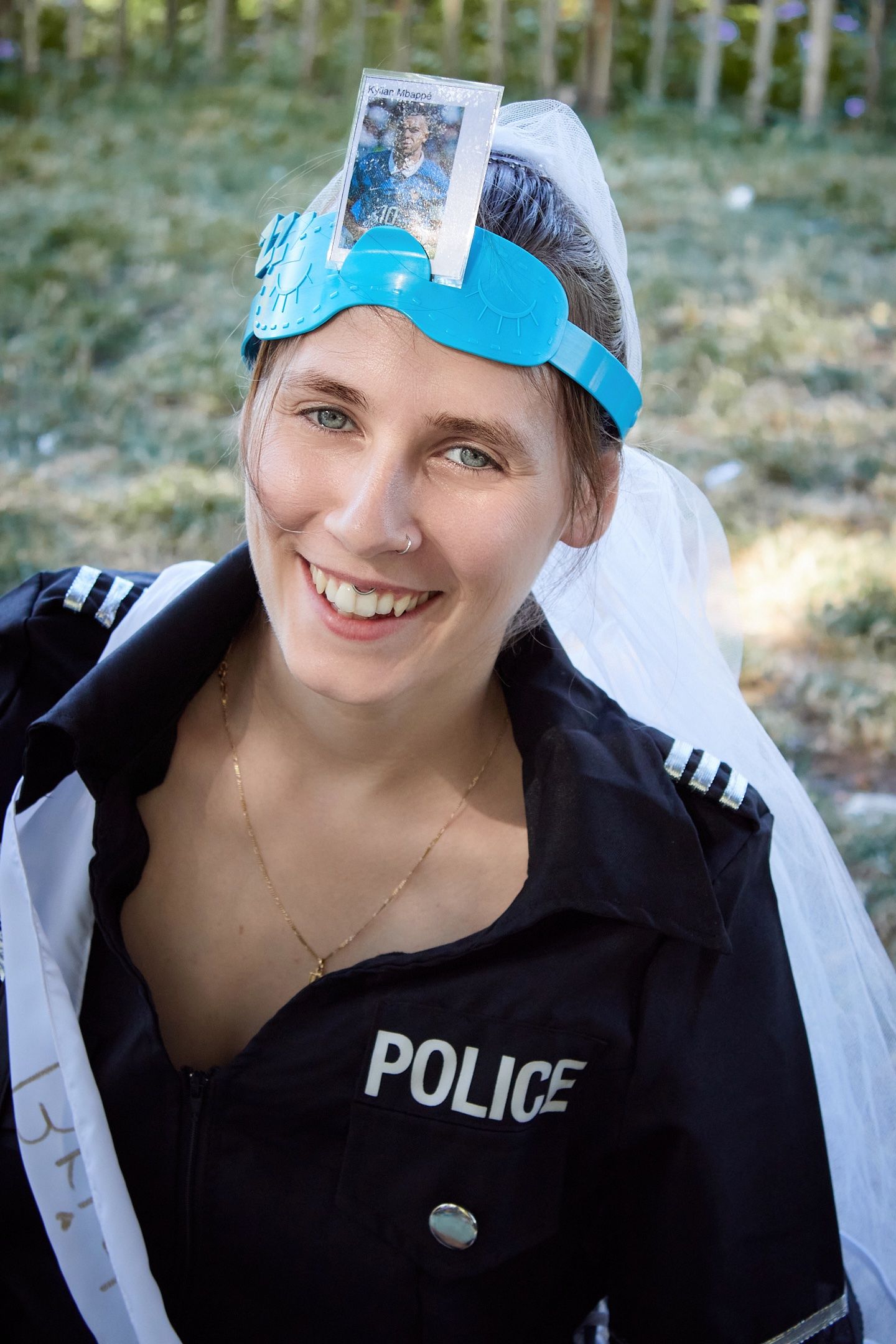 Smiling woman in a police costume with a blue tiara and veil, posing outdoors at a festive event.