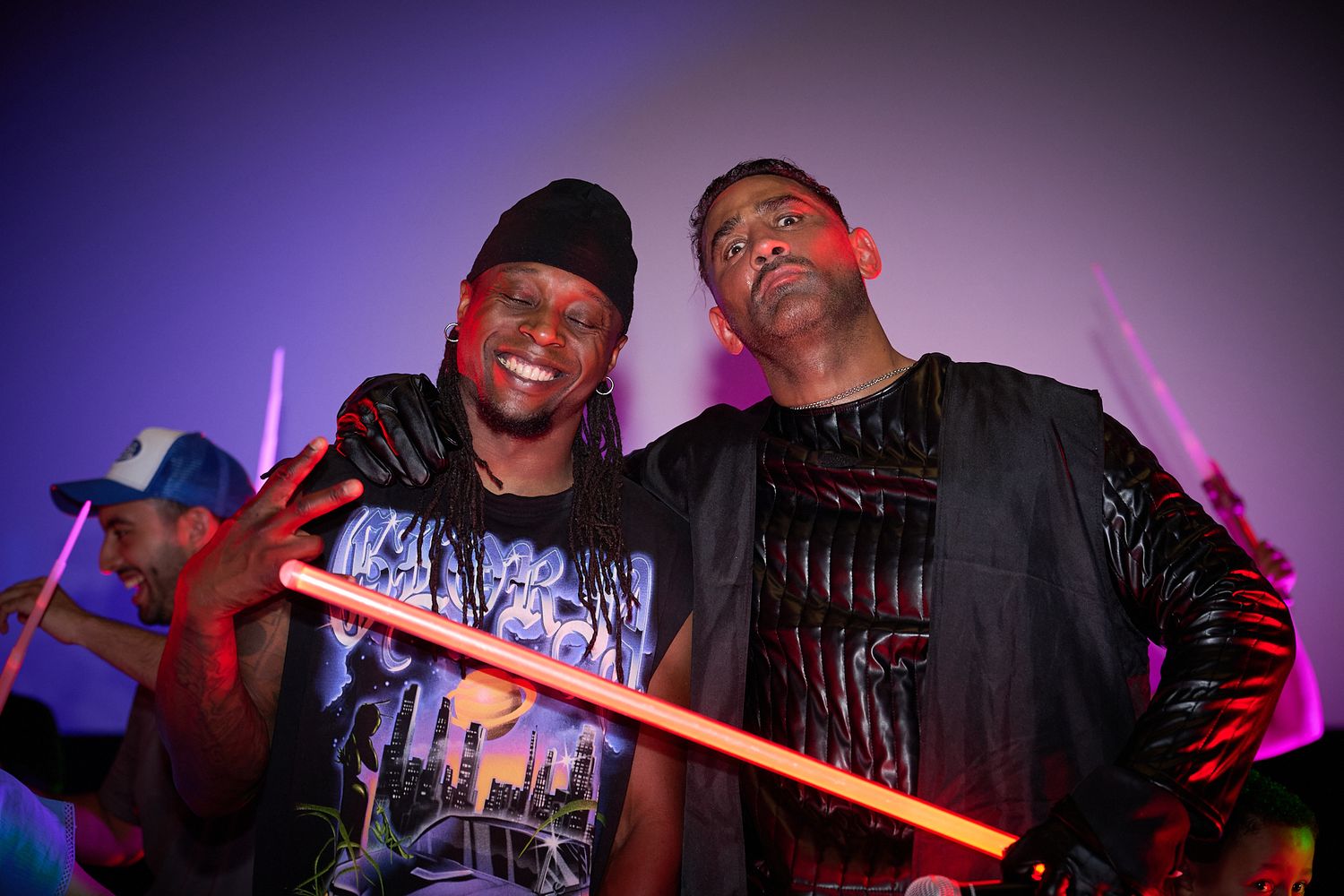Two men smiling and posing with colorful glow sticks at a vibrant nightclub party event.