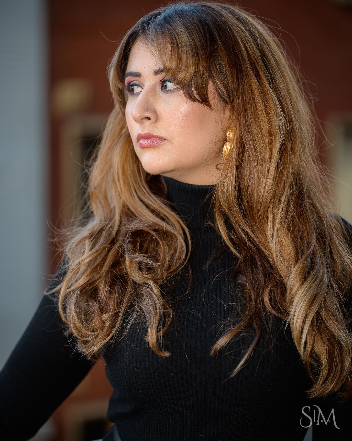 Close-up color portrait of a woman with wavy hair wearing gold earrings and a black turtleneck sweater.
