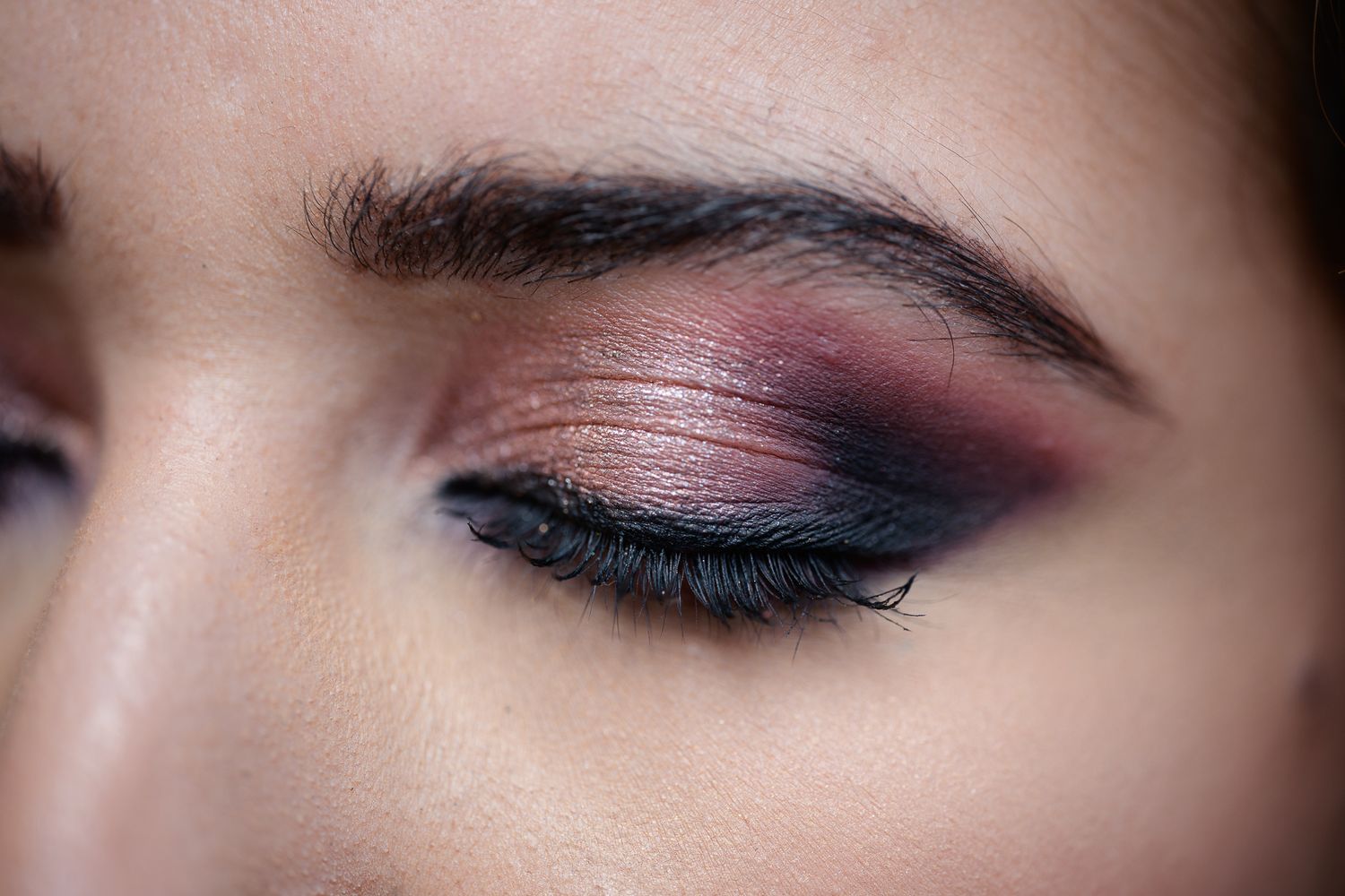 Close-up of a woman's eye with smoky pink and burgundy eyeshadow, bold eyeliner, and defined brows.