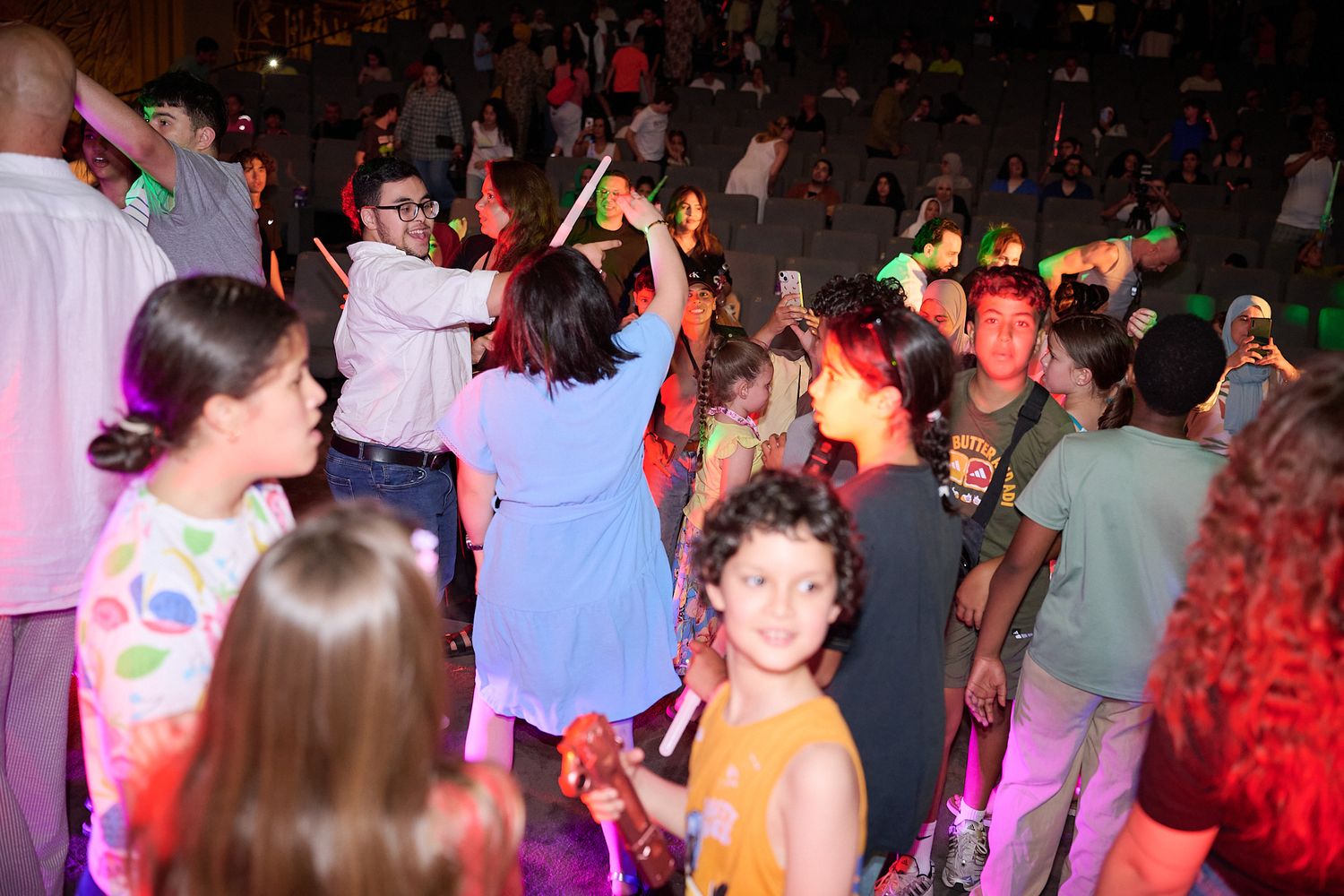 Children and adults dancing together at a colorful neon glow party event indoors.