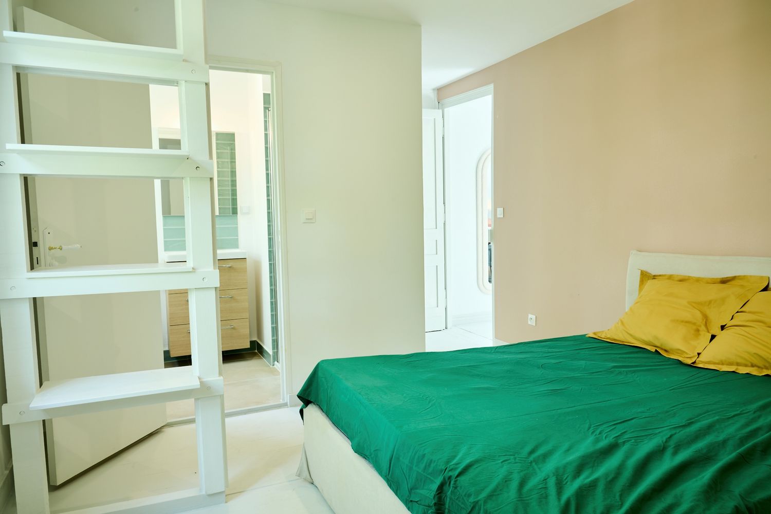 Modern bedroom with green bedspread, yellow pillows, white bunk bed ladder, and bright natural light from a door.