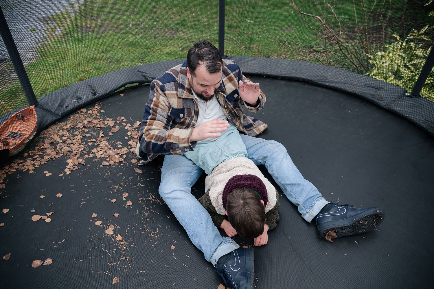 Father and child playing and wrestling together on a backyard trampoline.