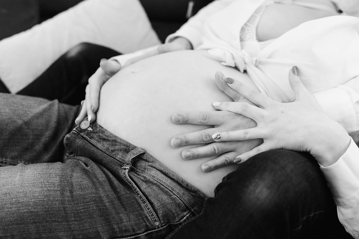 Black and white photo of pregnant woman cradling baby bump with both hands, wearing jeans and white top.