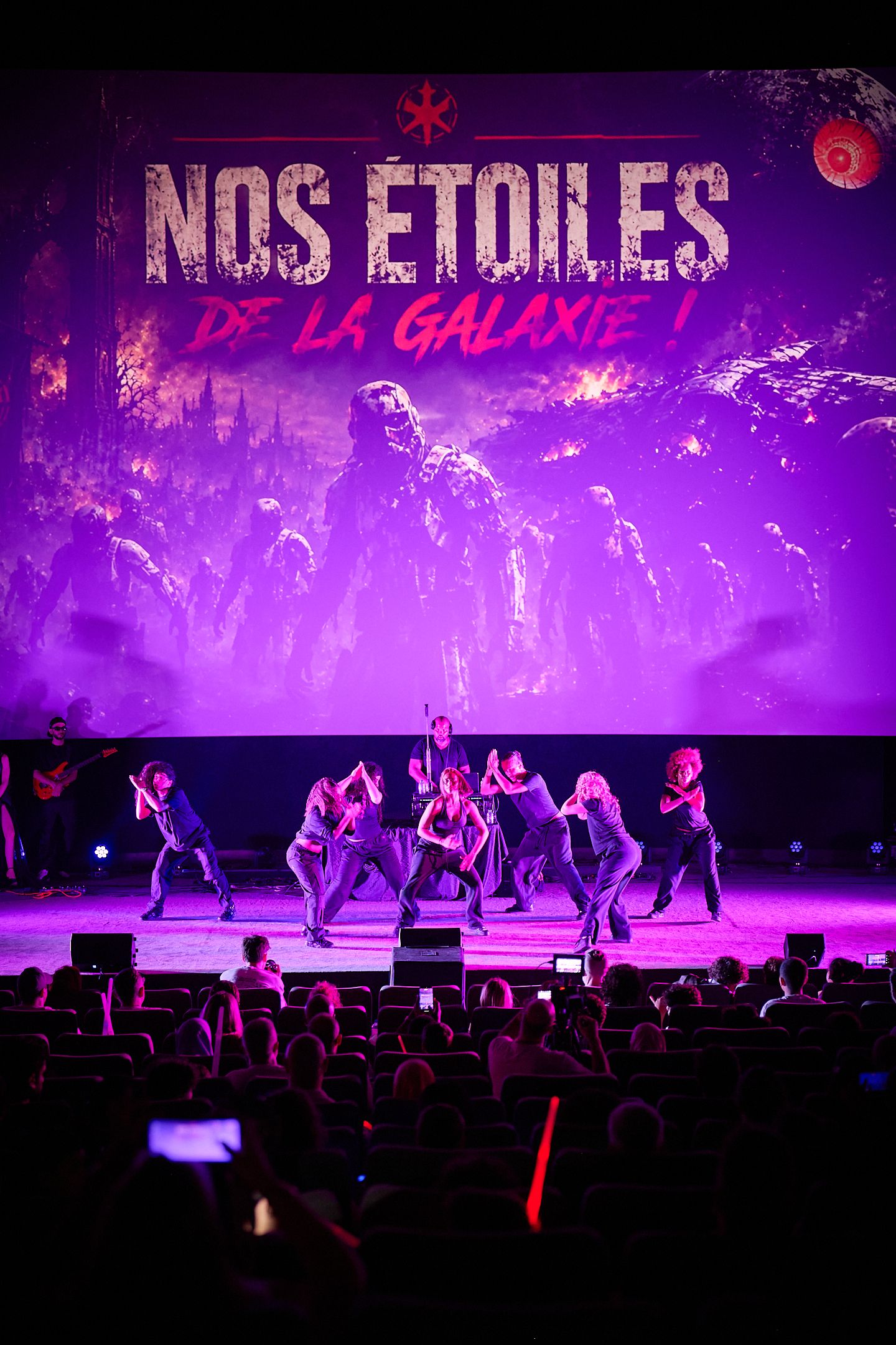 Dance performance on stage with purple lighting under 'Nos Etoiles de la Galaxie' projected backdrop.