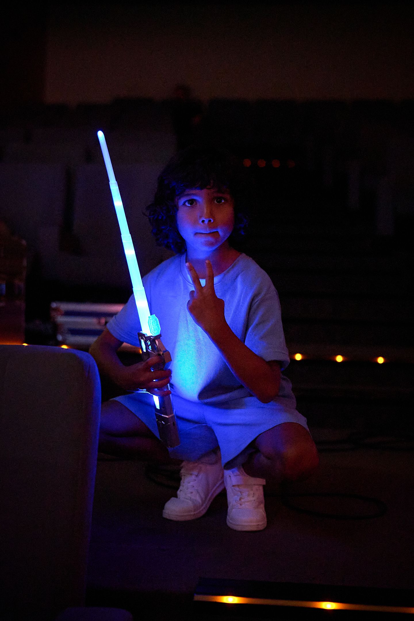 A child holds a glowing blue lightsaber toy in a dark room, illuminated by its blue light.