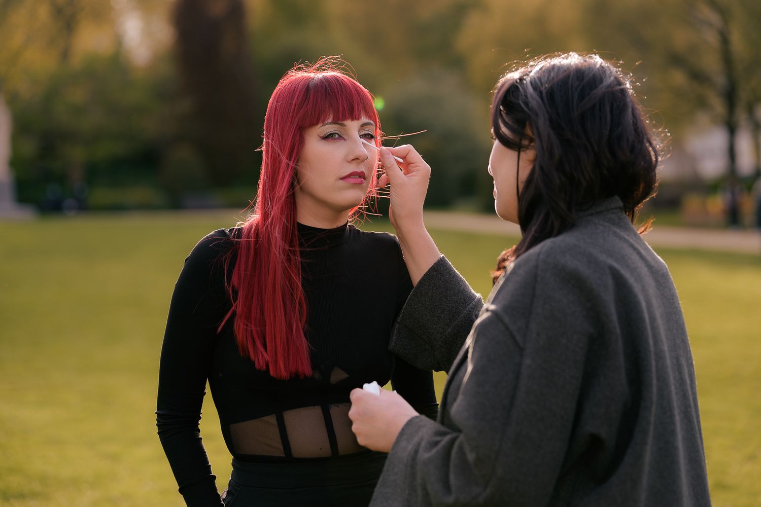Woman with red hair getting makeup applied outdoors in a park during golden hour.