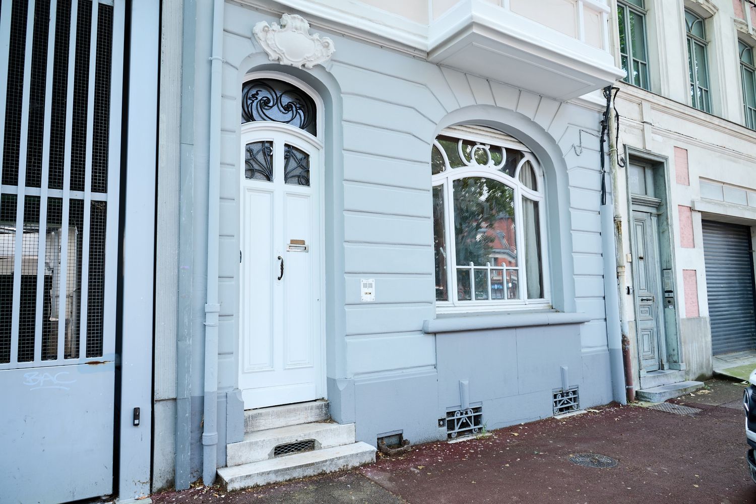 Historic European building facade with ornate white door, arched windows, and decorative moldings on a gray exterior wall.