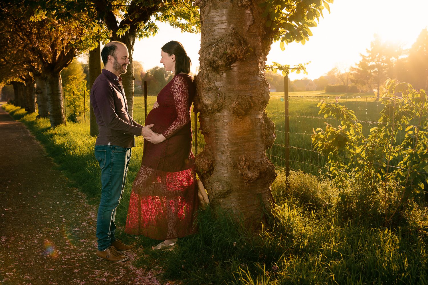 Pregnant couple sharing intimate moment by tree in golden sunset light in scenic park.