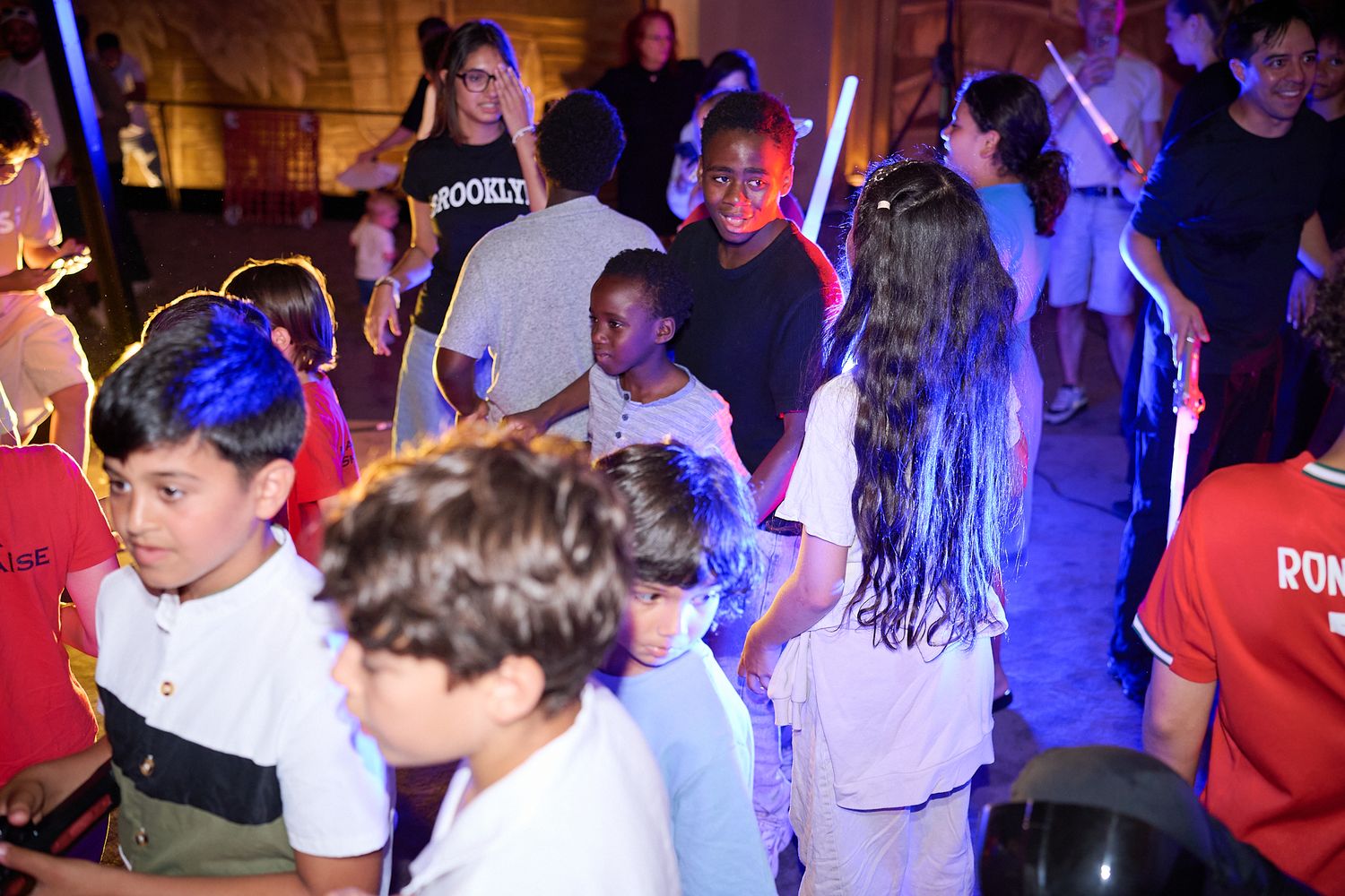 Children dancing and celebrating at a colorful indoor party event with glowing light sticks.