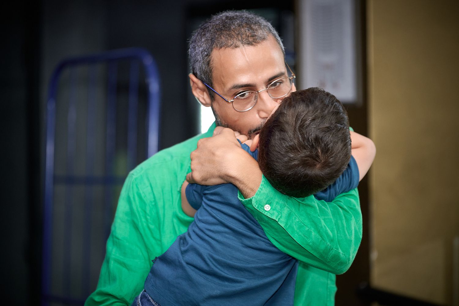 A man with glasses shares a warm embrace with a child in a heartfelt hug indoors.