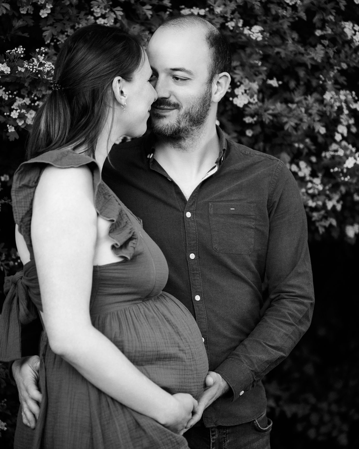 Black and white maternity photo of a couple sharing a tender moment outdoors, with woman's baby bump visible.
