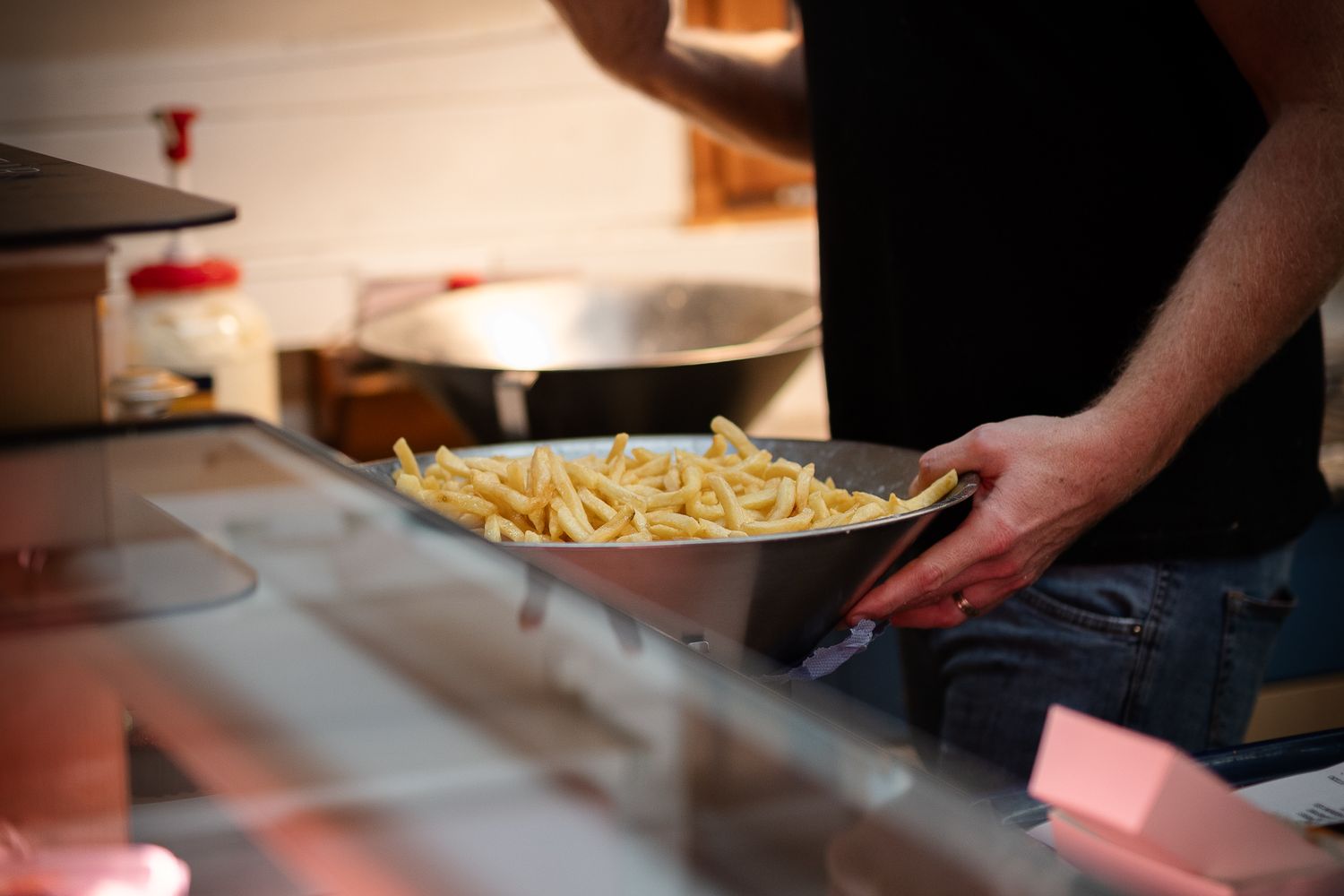 A chef holds a metal bowl filled with golden french fries in a restaurant kitchen setting.