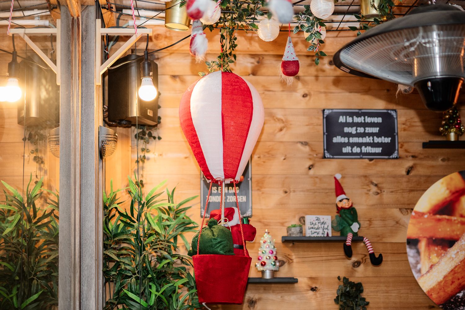 Festive indoor decor with a red and white hot air balloon ornament, elf figurines, and fairy lights on wooden walls.