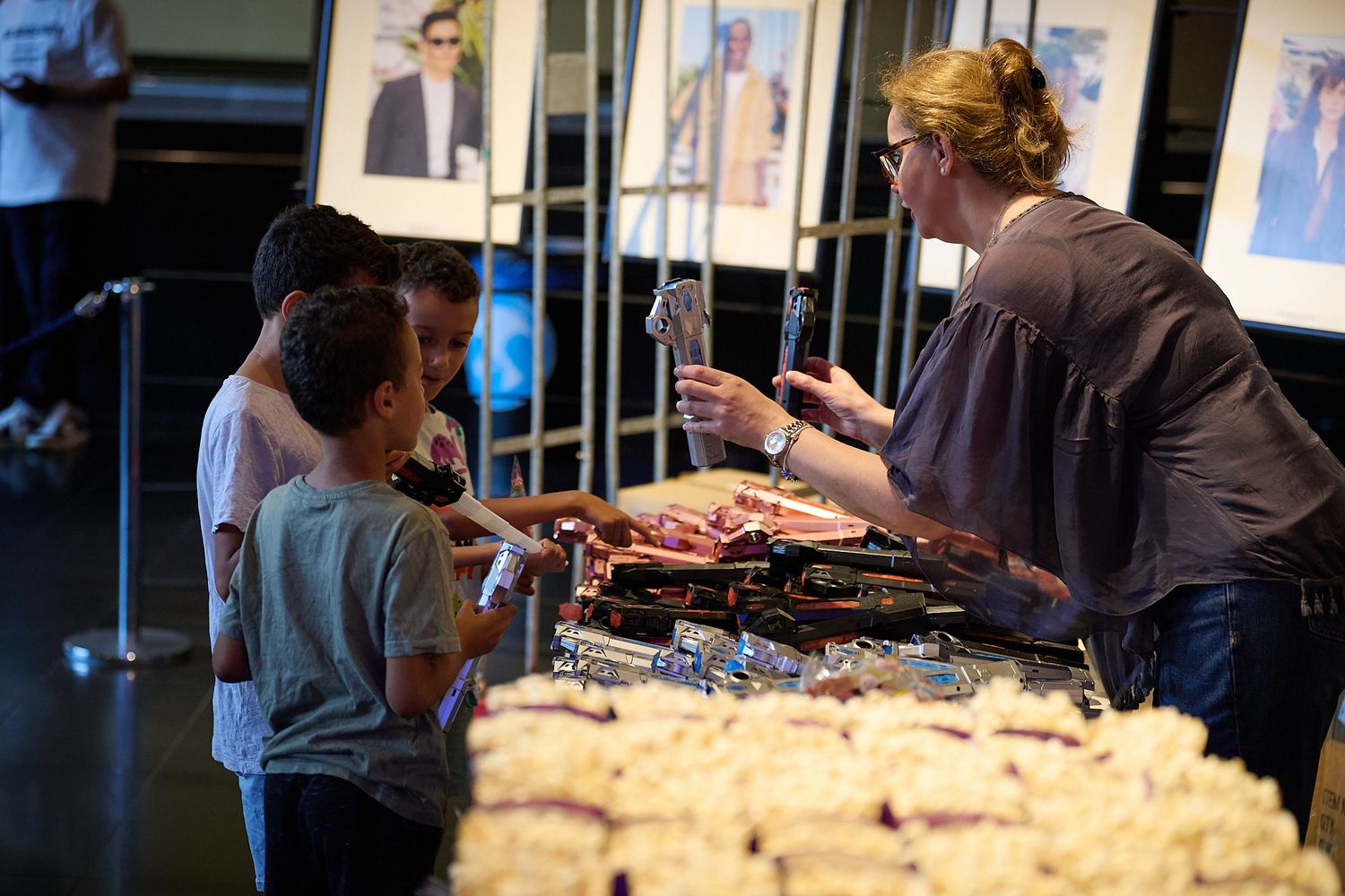 Children and woman serving food at a buffet table during an indoor event with photo displays in background.