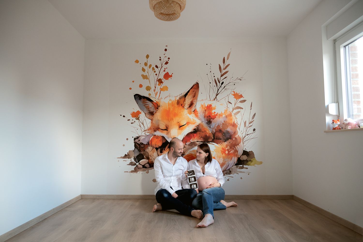 Two people sit on a floor in front of a large colorful fox wall mural with autumn floral accents in a bright room.