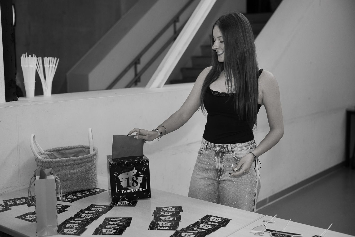 Young woman in black top and jeans arranging items on a decorated table at an event.